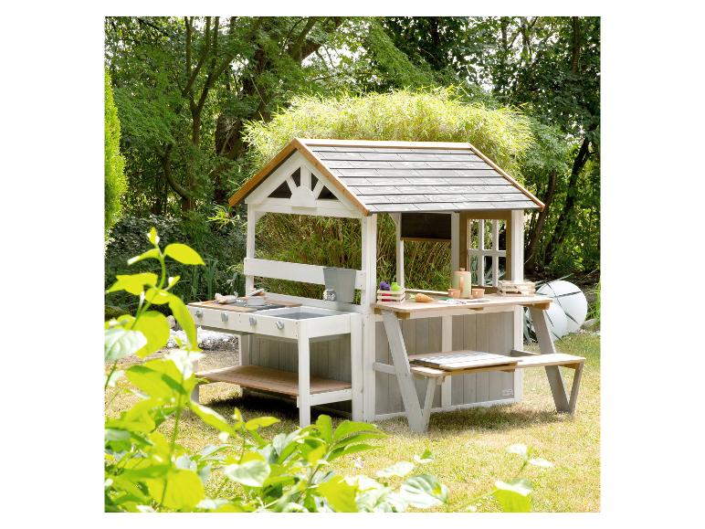 Ein Holzspielhaus mit Küche und Picknicktisch in einem grünen Garten.