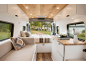 Van-Interieur mit Küche, Bett und Sofa, Blick auf einen Campingplatz am See.