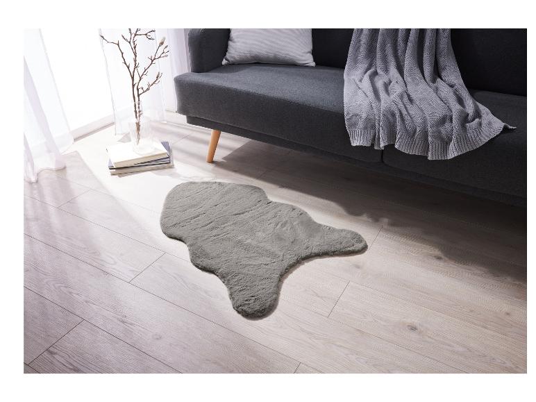 Ein grauer, flauschiger Teppich in Schafspelllook in einem Wohnzimmer mit einem Sofa.