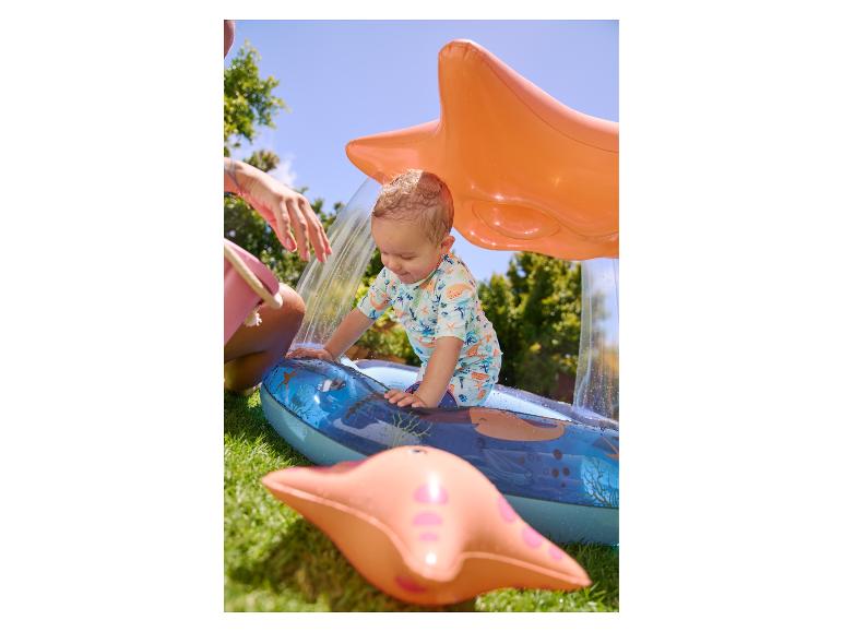 Baby spielt in einem aufblasbaren Planschbecken in Sternform mit Sprühfunktion.