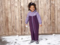 Ein Mädchen trägt einen lila Winteroverall und hält einen Schneeball.