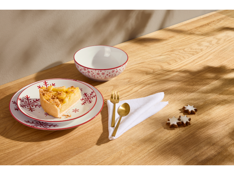 Weihnachtsteller mit einem Stück Kuchen, Schale und Keksen auf Holztisch.