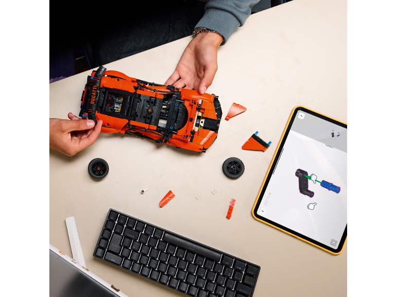Eine Person baut ein Spielzeug-Sportauto aus Klemmbausteinen mithilfe einer Anleitung auf einem Tablet.