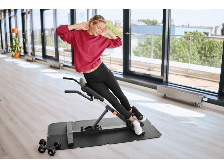 Eine Frau trainiert auf einem Rückentrainer in einem hellen Fitnessstudio.