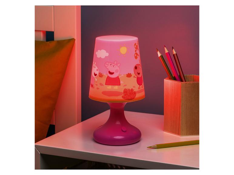 Rosa Kinderlampe mit Zeichentrickfiguren und einem Becher mit Buntstiften auf einem Tisch.