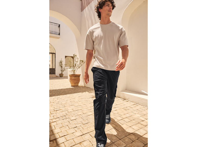 Mann trägt ein beiges T-Shirt und eine schwarze Hose in mediterraner Umgebung.