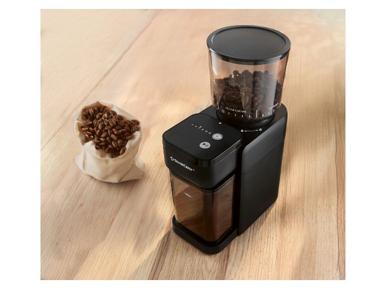 Schwarze SILVERCREST Kaffeemühle mit transparentem Bohnenbehälter und einem Beutel Kaffeebohnen.