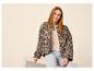 Frau in einer Leopardenjacke und hellen Jeans sitzt auf einem weißen Podest.