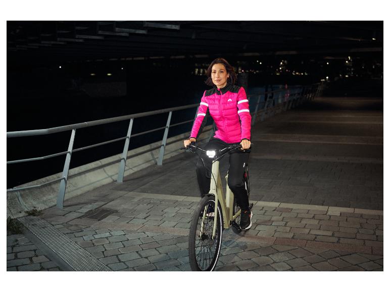 Frau in pinker Fahrradjacke fährt nachts ein E-Bike.