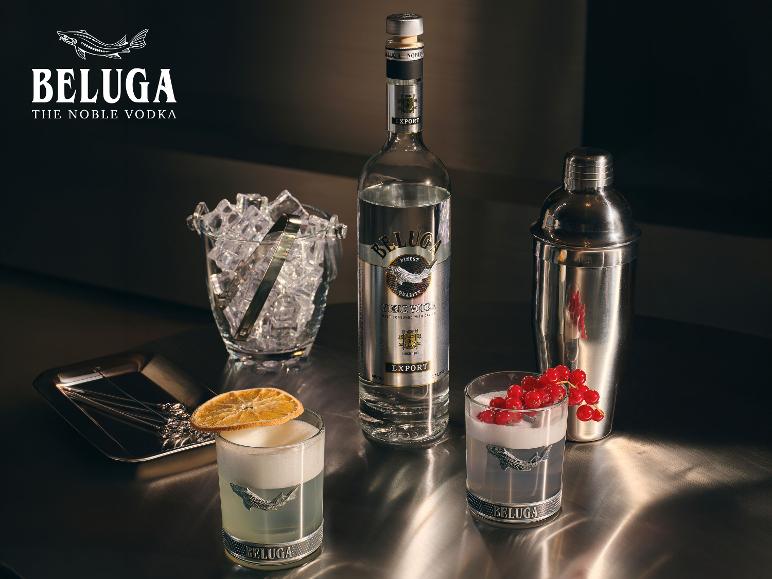 Wodkaflasche, Eiseimer, Cocktailshaker und zwei Cocktails mit Garnituren auf einer Metalloberfläche.