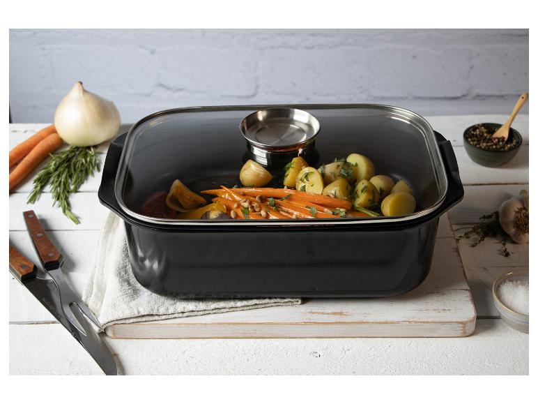 Schwarzer Bräter mit Glasdeckel, gefüllt mit geröstetem Gemüse, auf einem Holzbrett.