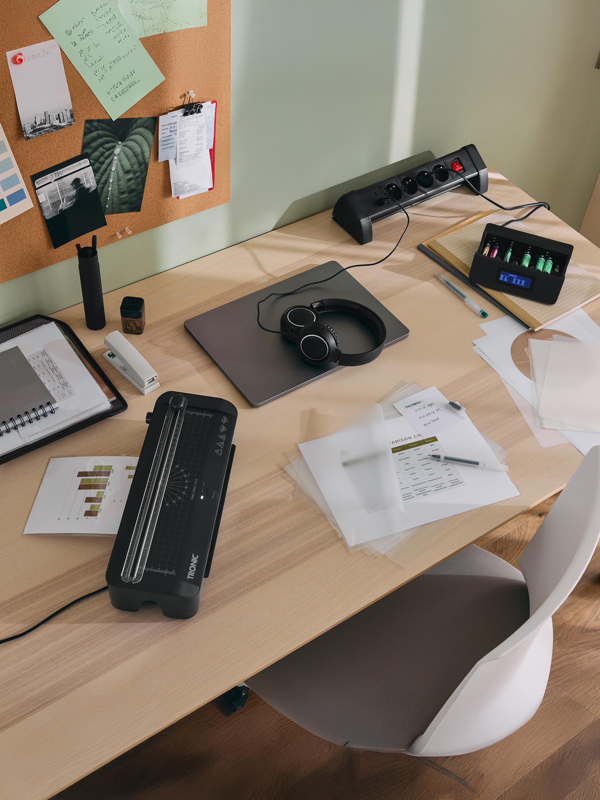 Schreibtisch mit TRONIC Laminiergerät, Akkuladegerät, Laptop, Kopfhörern und Büromaterial.