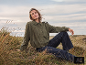 Frau in grüner Jacke und dunklen Jeans sitzt auf einem Grasfeld.