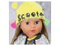 Puppe mit gelber „Scooter“-Mütze und glitzernder Jacke.