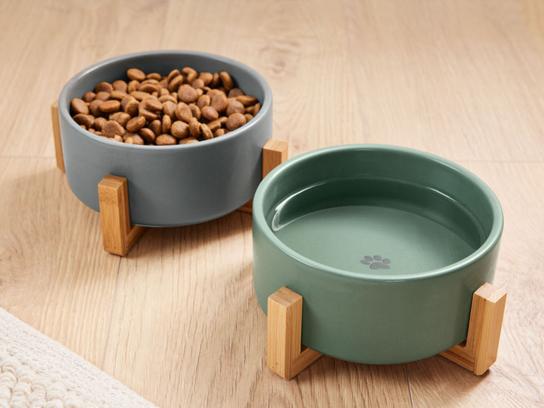Zwei Keramiknäpfe für Hunde auf einem Holzständer, einer mit Futter, einer mit Wasser.