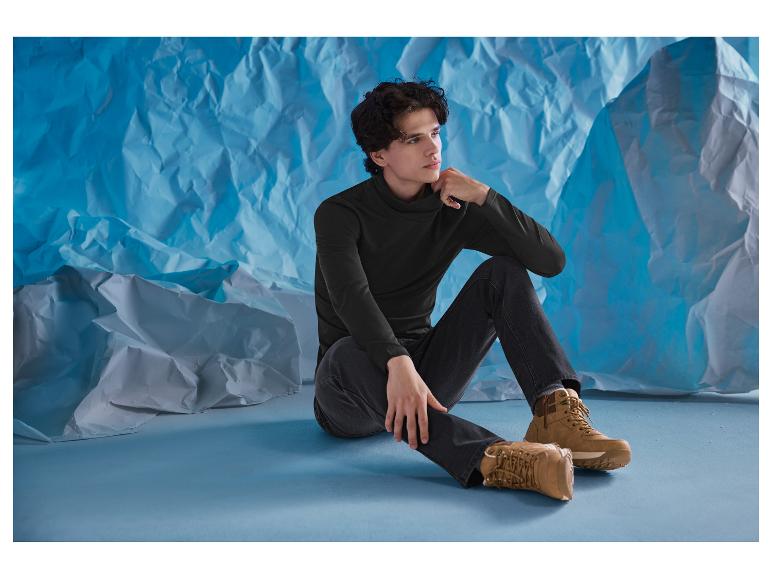 Mann in schwarzem Rollkragenpullover und Jeans sitzt auf dem Boden mit braunen Stiefeln.