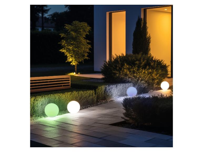 Gartenkugelleuchten beleuchten einen Weg und Büsche vor einem Haus bei Nacht.