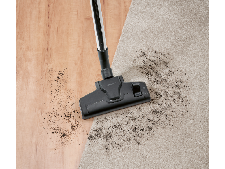 Staubsauger auf Holzboden und Teppich mit Schmutz.