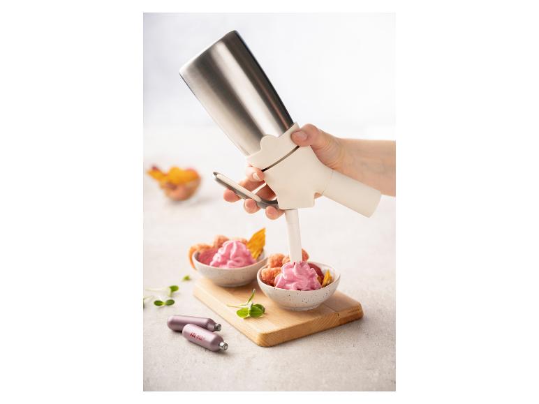 Sahnespender füllt rosa Sahne in eine Obstschale, mit Kartuschen auf dem Tisch.