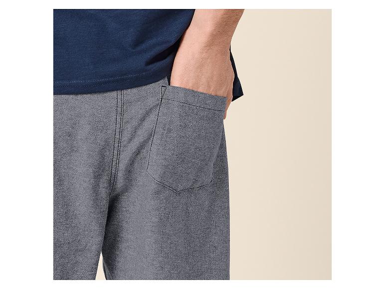 Mann in blauem T-Shirt und grauen Shorts mit der Hand in der Tasche.