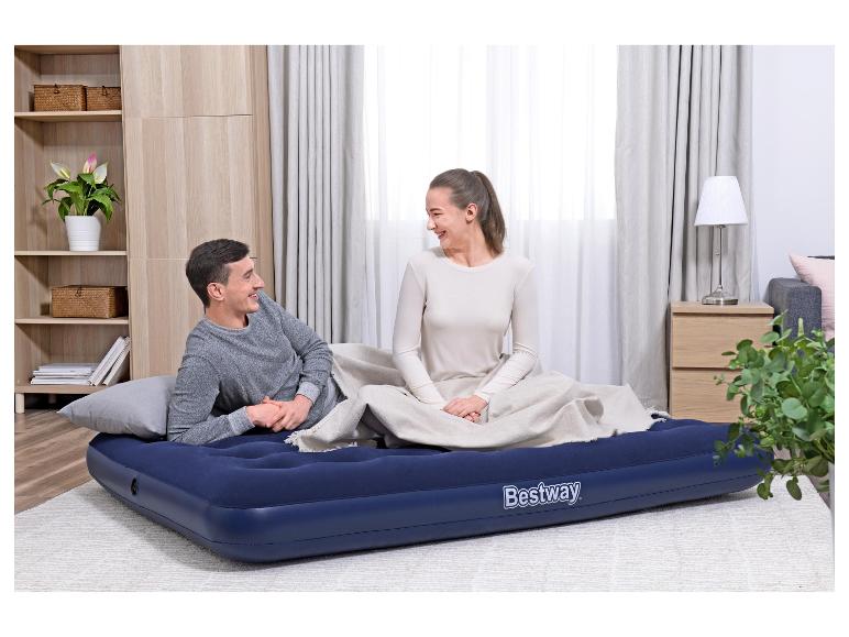Lächelndes Paar entspannt auf einer blauen Bestway Luftmatratze auf dem Wohnzimmerboden.