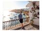 Mann in Poloshirt und Shorts auf einem Balkon mit Meerblick und Booten.