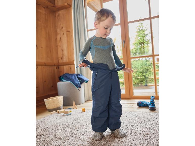 Ein Junge in einem grauen Thermo-Unterhemd und blauen Skihosen