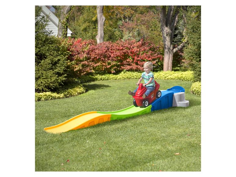 Kind in rotem Spielzeugauto fährt eine bunte Achterbahnstrecke im Garten hinunter.