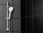 Eine verchromte Duschbrause und -stange vor einer schwarzen Fliesenwand.