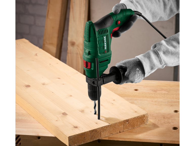 Schlagbohrmaschine in Händen, bohrt in ein Holzbrett auf einer Werkbank.