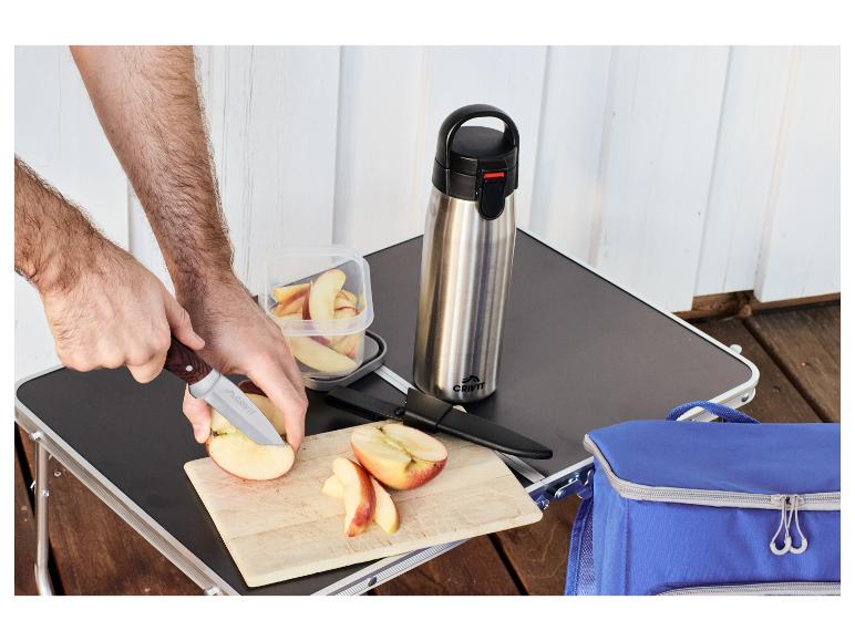Mann schneidet Äpfel auf einem Picknicktisch mit Thermosflasche und Kühltasche.
