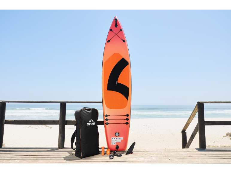 Orangefarbenes Paddleboard mit Zubehör und Tasche auf einem Holzsteg am Strand.