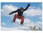 Snowboarder in schwarzer Jacke und orangefarbener Hose schwebt in der Luft vor blauem Himmel.