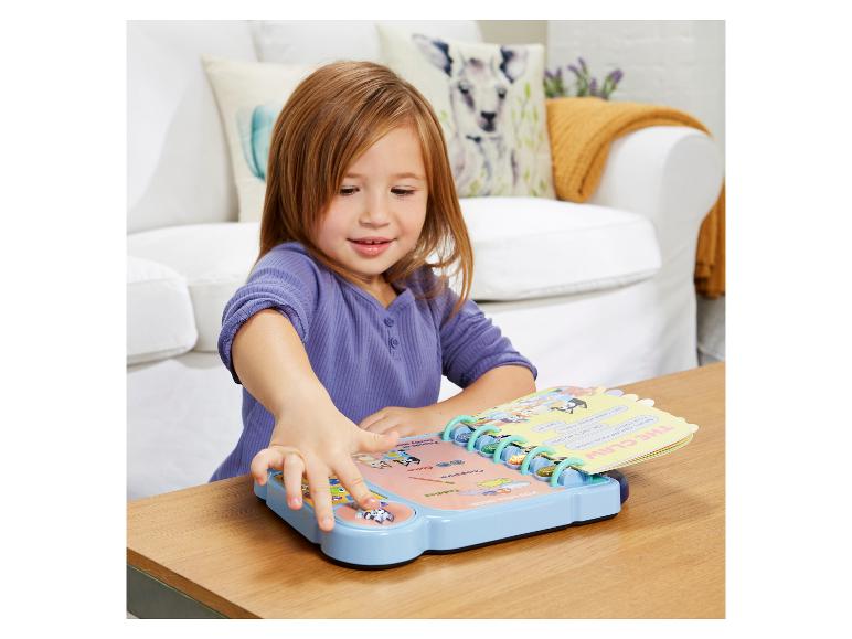 Mädchen spielt mit einem interaktiven Soundbuch auf einem Holztisch.