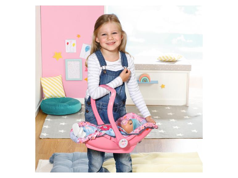 Mädchen hält einen rosa Puppenautositz mit einer Puppe, in einem Kinderzimmer.