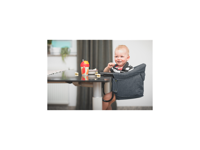 Lächelndes Baby in einem Tischsitz, mit Becher und Snacks.