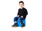 Junge in schwarzem Pullover, Jeans und blauen Stiefeln sitzt auf einem blauen Hocker.