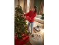Frau schmückt Weihnachtsbaum mit Kugeln und Geschenken im Wohnzimmer.