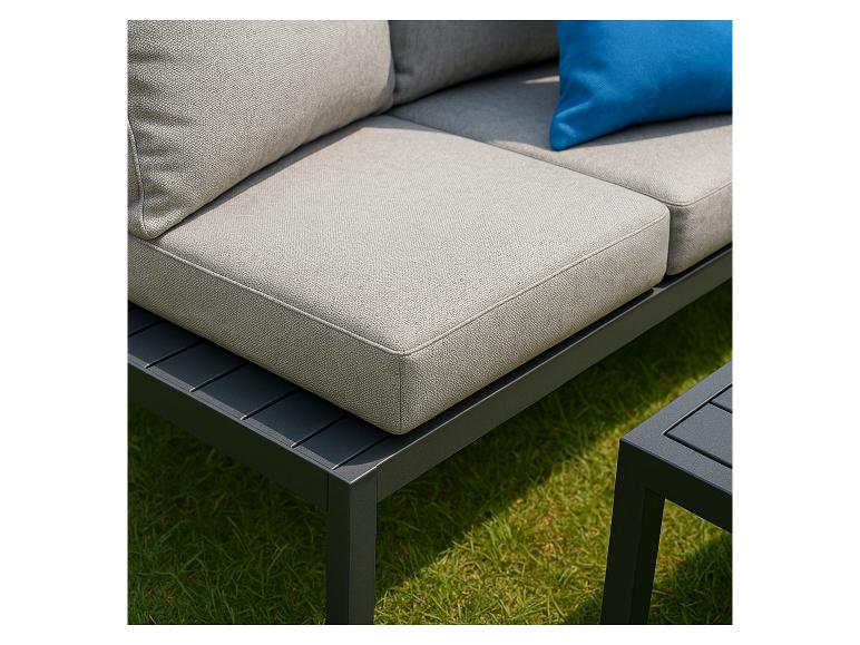 Gartensofa mit grauen Kissen und einem blauen Zierkissen, auf grünem Rasen.
