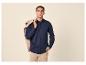 Mann in marineblauem Button-Down-Hemd und beiger Hose, beigefarbene Jacke über der Schulter.