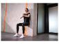 Frau in schwarzer Sportkleidung und weißen Sportschuhen macht einen Wall Sit.