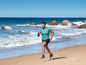 Mann läuft in Sportkleidung an einem Sandstrand.