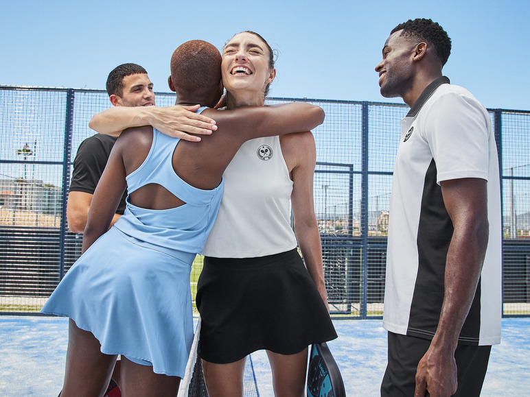 Zwei Frauen in Tennisbekleidung umarmen sich auf einem Tennisplatz.