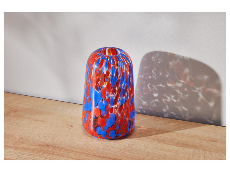 Eine blaue und rote Glasvase mit Punkten auf einem Holztisch.