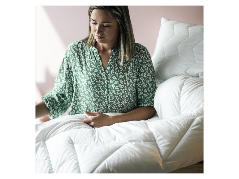 Frau in grünem Blumenhemd, die eine flauschige weiße Bettdecke hält.