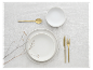 Weißes Geschirr, goldenes Besteck und minimalistische Dekoration.