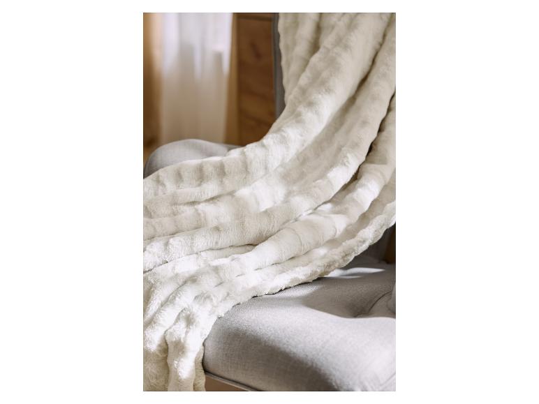 Weiche, gemütliche cremefarbene Kunstpelzdecke auf einem grauen Sessel.