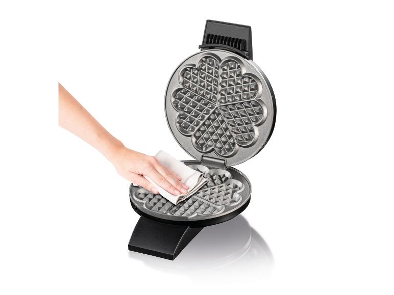 Hand reinigt Waffeleisen mit einem Tuch auf weißem Hintergrund.