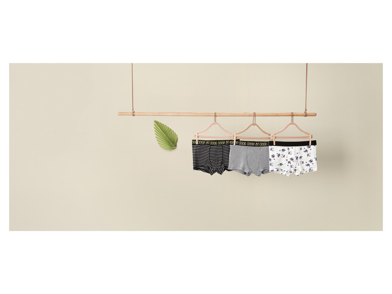 Drei Boxershorts mit 'Keep it Cool'-Druck, die an einem Holzgestell hängen.