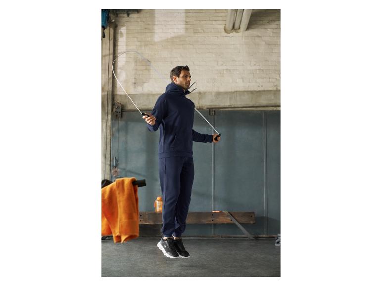 Mann in marineblauem Trainingsanzug und schwarzen Turnschuhen beim Seilspringen im Fitnessstudio.